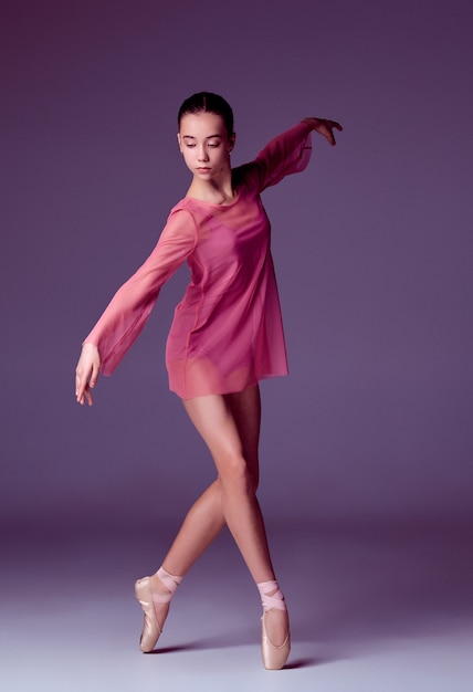 Jonge ballerinadanseres in roze jurk die haar technieken toont op lila achtergrond