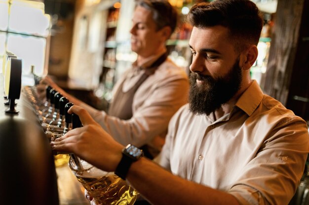 Jonge barista en zijn collega schenken tapbier uit de biertap in een pub