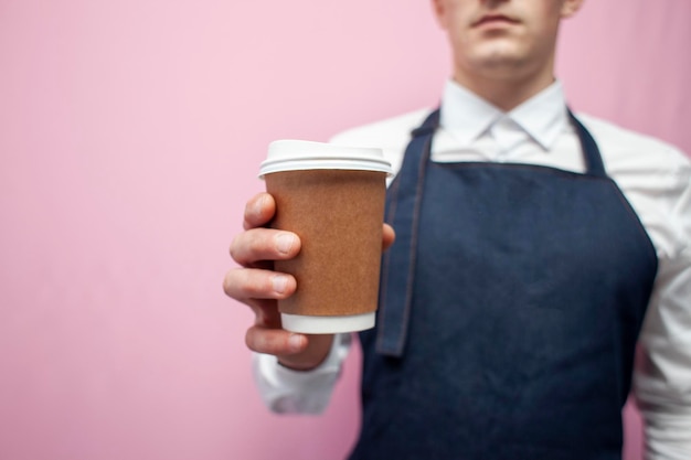 Jonge barista in wit overhemd en schort houdt kopje koffie op roze achtergrond