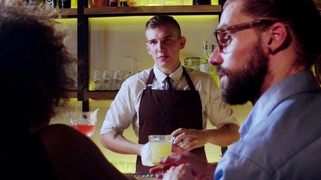 Jonge barman op het werk neemt bestellingen op terwijl hij met klanten praat