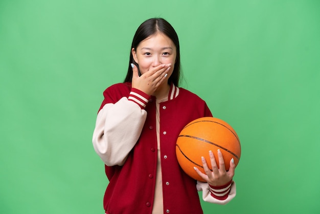 Jonge basketbalspeler aziatische vrouw over geïsoleerde achtergrond gelukkig en glimlachend die mond met hand bedekken