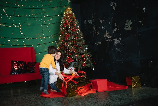 Jonge beautyful moeder met de schattige zoon in de buurt van kerstboom met geschenken. vrolijk kerstfeest