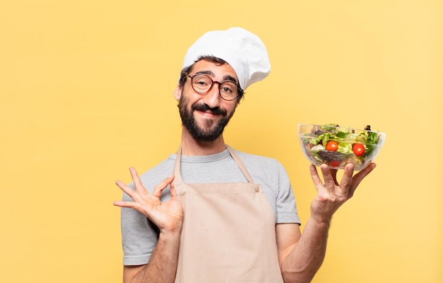 Jonge, bebaarde chef-kok man gelukkige uitdrukking en met een salade