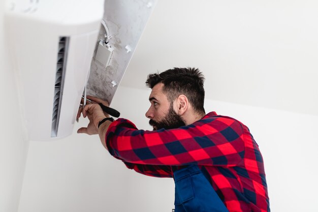 Jonge, bebaarde klusjesman die airconditioner repareert.