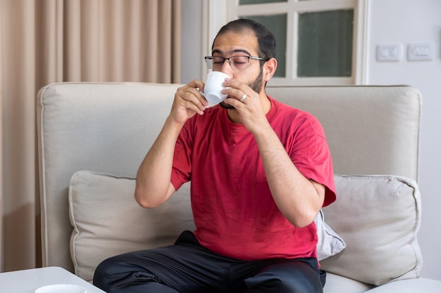 Jonge, bebaarde man die koffie drinkt en glimlacht in de woonkamer