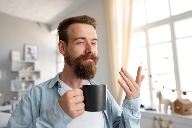 Jonge, bebaarde man die thuis lacht en koffie drinkt