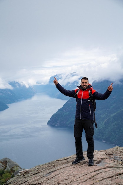 Jonge, bebaarde man die zijn handen opsteekt met Lysefjord-fjord op het achtergrondconcept van succes en zelfverbetering