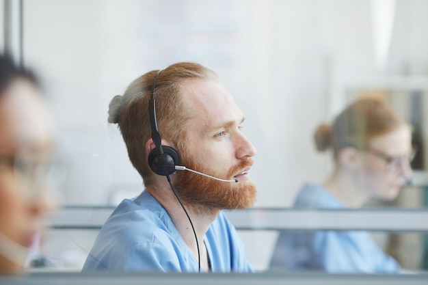 Jonge, bebaarde man in koptelefoon werken in medisch callcenter