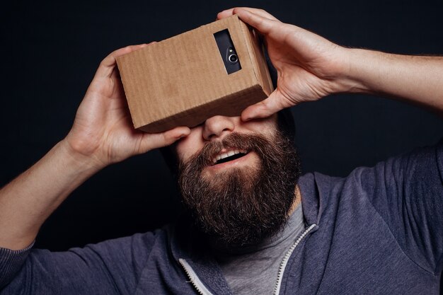 Jonge, bebaarde man kijkt door een kartonnen VR-headset