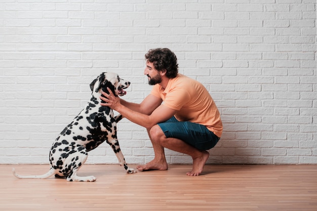 Jonge, bebaarde man met een Dalmatische hond tegen witte bakstenen muur