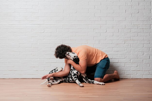 Jonge, bebaarde man met een Dalmatische hond tegen witte bakstenen muur