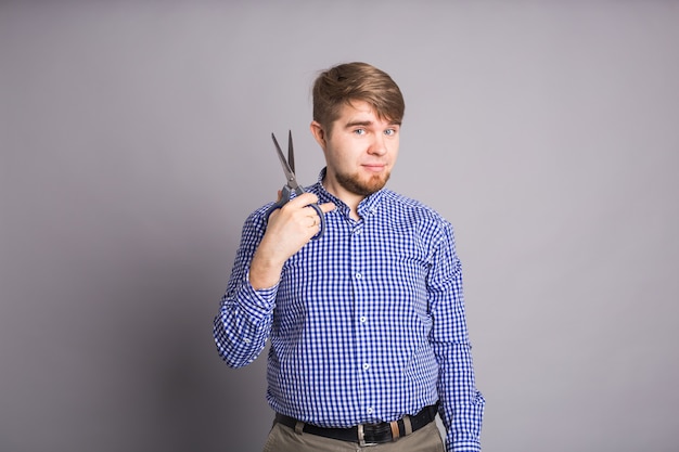 Jonge, bebaarde man met een schaar op grijze muur