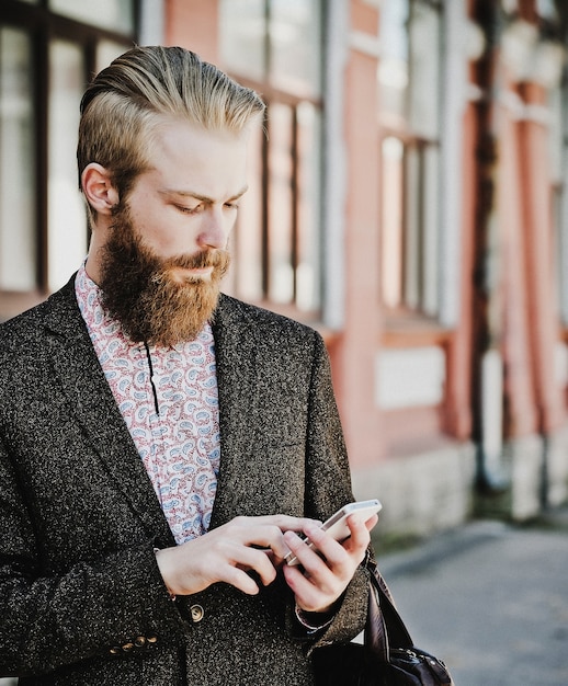 Jonge, bebaarde man met mobiel, buiten, zomertijd