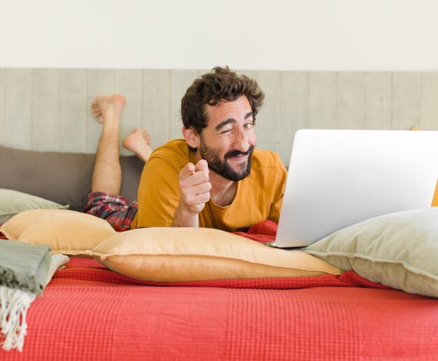 Jonge, bebaarde man op een bed met een laptop