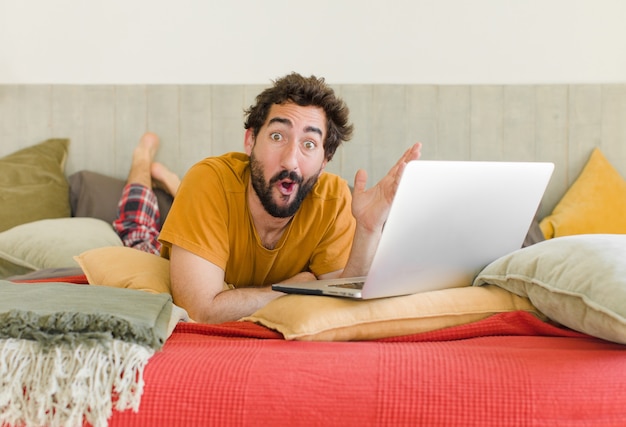 Jonge, bebaarde man op een bed met een laptop