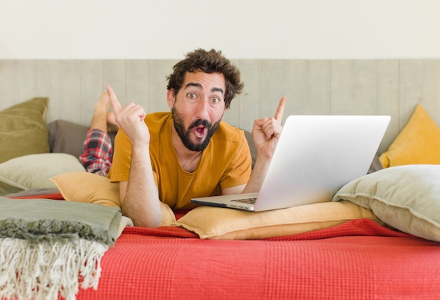 Jonge, bebaarde man op een bed met een laptop
