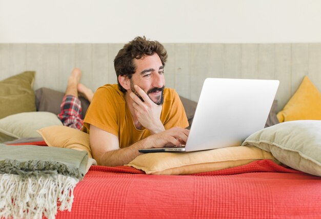 Jonge, bebaarde man op een bed met een laptop