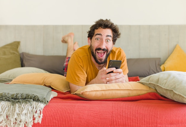 Jonge, bebaarde man op een bed met zijn mobiele telefoon