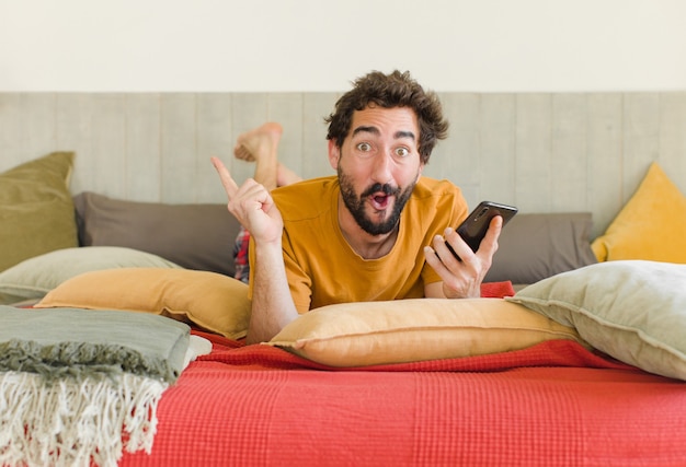 Jonge, bebaarde man op een bed met zijn mobiele telefoon