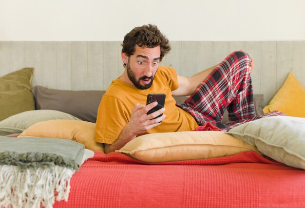 Jonge, bebaarde man op een bed met zijn mobiele telefoon