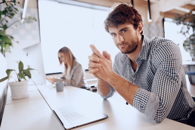 Jonge, bebaarde succesvolle zakenman die op laptop in bureau met vrouwelijke collega werkt