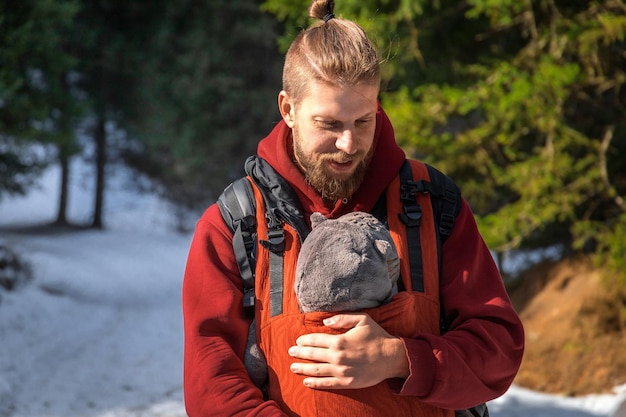 Jonge, bebaarde vader met zijn zoontje in ergonomische draagzak in de winter buiten