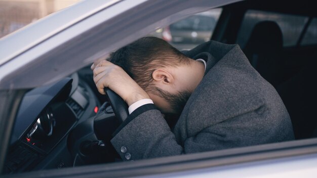Jonge, bebaarde zakenman die in de auto zit, erg overstuur en gestrest na een harde mislukking