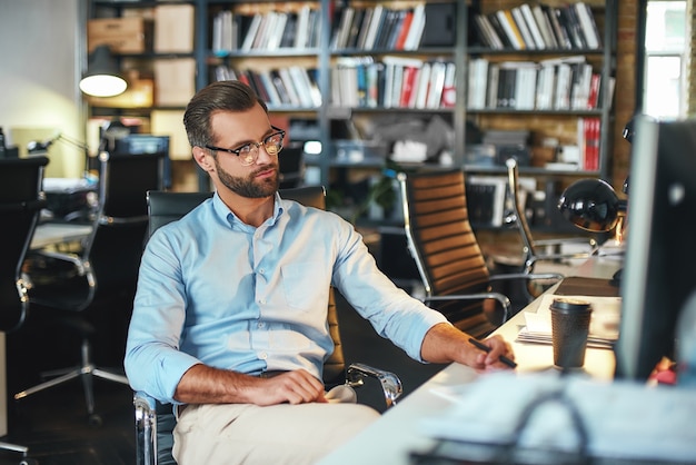 Jonge, bebaarde zakenman in brillen en formele kleding die op de computer werkt