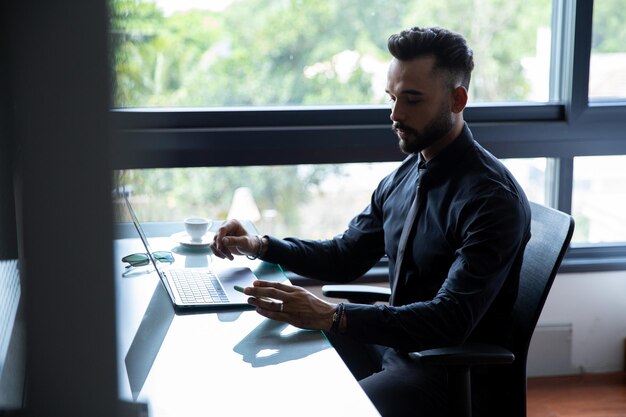 Jonge, bebaarde zakenman zit in zijn kantoor aan huis, voor zijn computertechnologie thuiskantoor