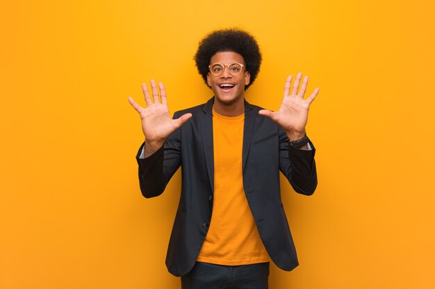 Foto jonge bedrijfs afrikaanse amerikaanse mens over een oranje muur die nummer tien toont