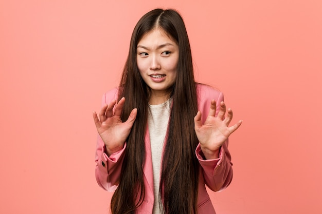 Jonge bedrijfs chinese vrouw die roze kostuum draagt dat iemand verwerpt die een gebaar van walging toont.