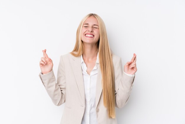 Jonge bedrijfsblonde vrouw op witte muur die vingers kruisen voor het hebben van geluk