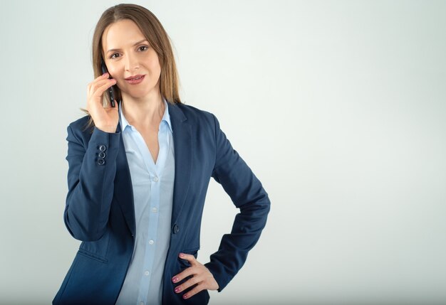 Jonge bedrijfsdame spreekt op een celtelefoon die op grijze achtergrond wordt geïsoleerd