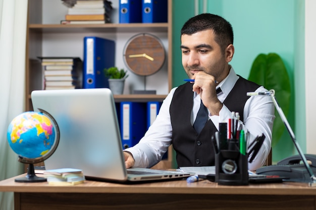 Jonge bedrijfsmens die aan laptop bij lijst in bureau werkt