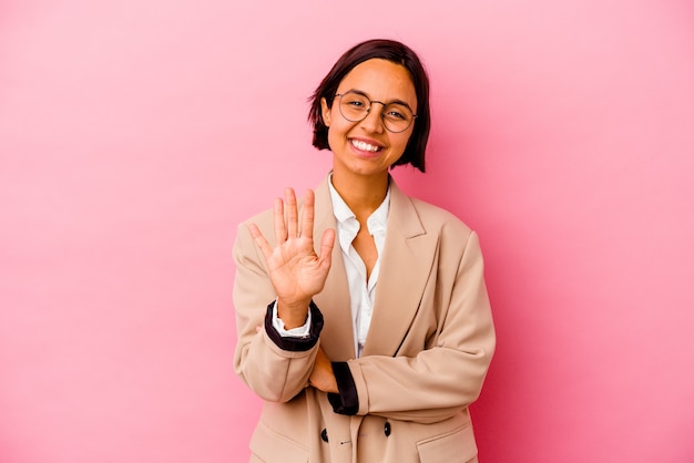 Jonge bedrijfsvrouw die op roze muur wordt geïsoleerd die vrolijk glimlachend nummer vijf toont met vingers