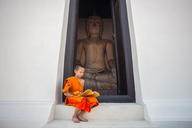 Jonge beginnende monnik die een boek leest in de tempel van Wat Phutthai Sawan, Ayutthaya, Thailand