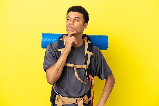 Jonge bergbeklimmer Afro-Amerikaanse man met een grote rugzak geïsoleerd op gele achtergrond en opzoeken