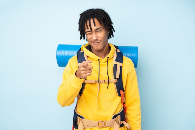 Jonge bergbeklimmer Afro-Amerikaanse man met een grote rugzak op een blauwe muur wijst