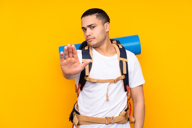 Jonge bergbeklimmer Aziatische man met een grote rugzak geïsoleerd op geel stop gebaar met haar hand maken