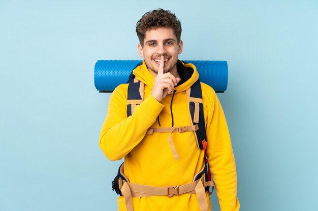 Jonge bergbeklimmer man met een grote rugzak geïsoleerd op blauw stilte gebaar doen