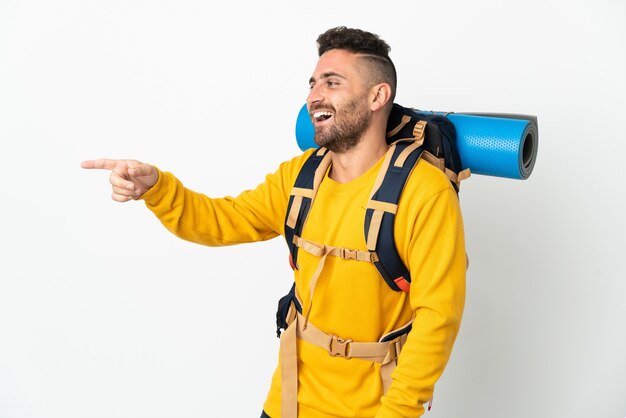 Jonge bergbeklimmer man met een grote rugzak over geïsoleerde achtergrond wijzende vinger naar de zijkant en presenteert een product