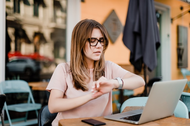 Jonge betrokken vrouw die tijd controleert en laptop voor het freelance werk in het koffie met behulp van