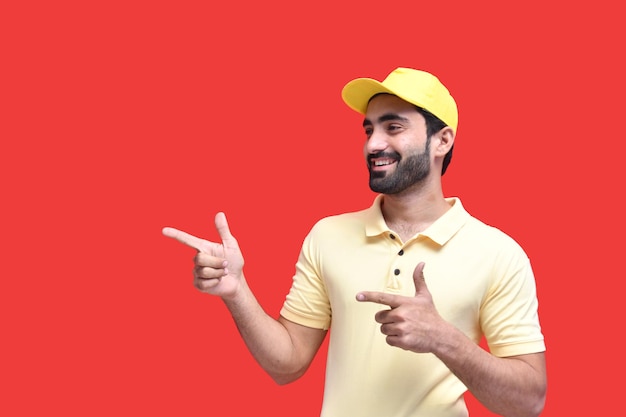 jonge bezorger in geel t-shirt en pet glimlachend opzij wijzend naar het Indiase Pakistaanse model