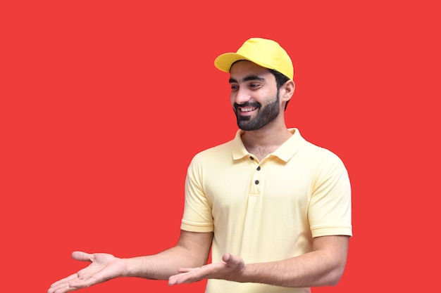 jonge bezorger vooraanzicht in geel t-shirt glimlachend over rode achtergrond indain pakistaans model