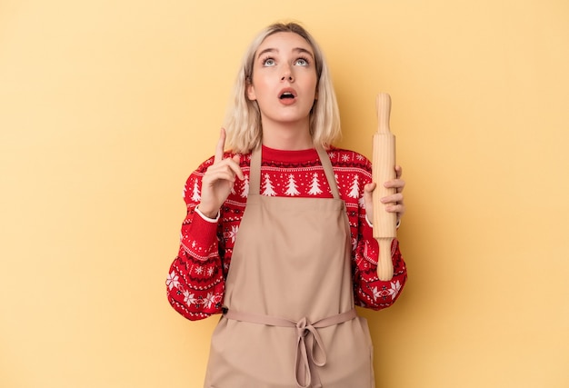 Jonge blanke bakkersvrouw die koekjes doet voor Kerstmis geïsoleerd op een gele achtergrond die ondersteboven wijst met geopende mond.