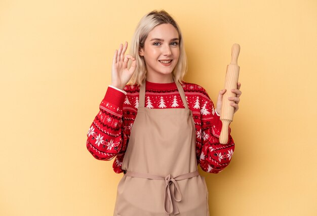 Jonge blanke bakkersvrouw die koekjes doet voor Kerstmis geïsoleerd op een gele achtergrond, vrolijk en zelfverzekerd met een goed gebaar.