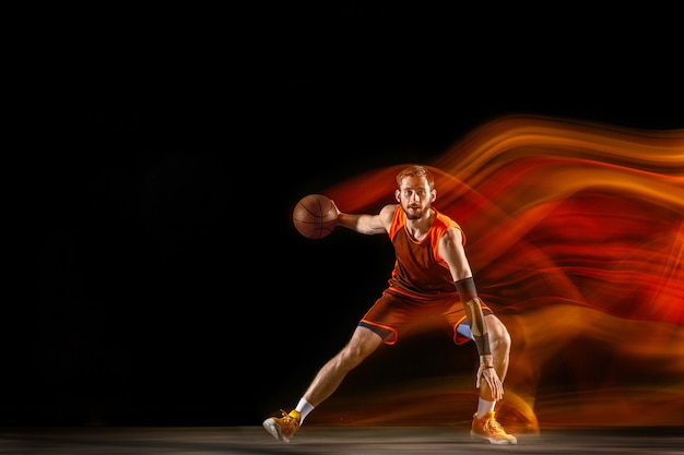 Jonge blanke basketbalspeler tegen een donkere achtergrond in gemengd licht