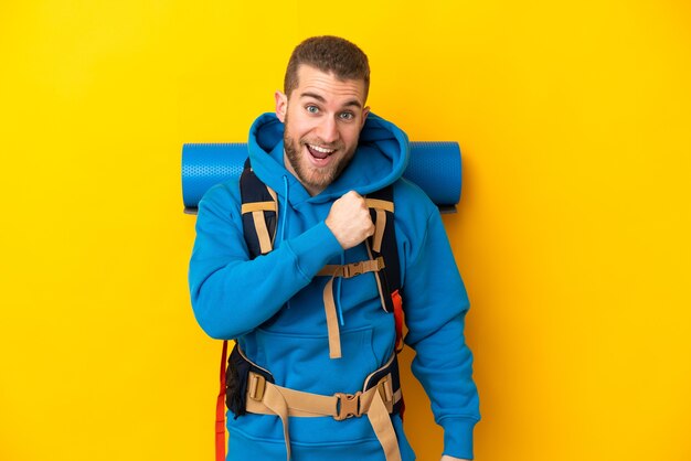 Jonge blanke bergbeklimmer man met een grote rugzak geïsoleerd op geel een overwinning vieren