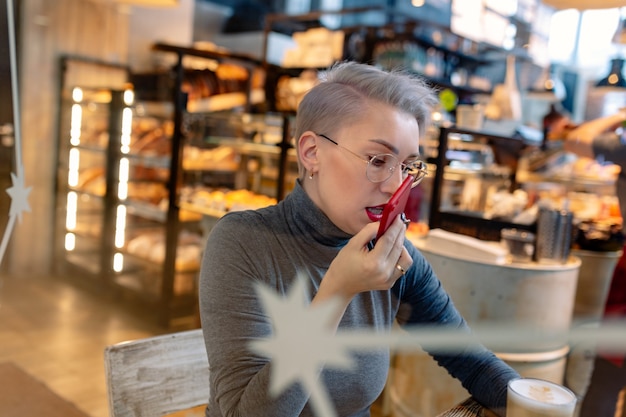 jonge blanke blonde vrouw die audiobericht opneemt met smartphone die in café zit