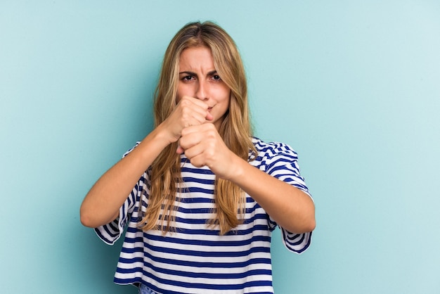 Foto jonge blanke blonde vrouw geïsoleerd op blauwe achtergrond die een vuistslag gooit, woede, vecht vanwege een ruzie, boksen.